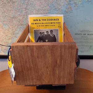 May include: A wooden record holder with a vintage album titled "IAN & THE ZODIACS SO MUCH IN LOVE WITH YOU" displayed inside. The album cover is yellow with a black and white photo of the band. The holder is made of light brown wood.