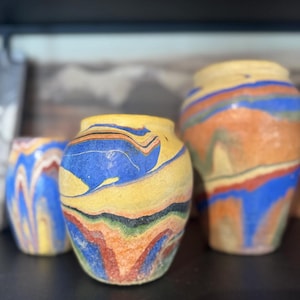 Könnte beinhalten: Drei Keramikvasen mit einem farbenfrohen Wirbeldesign. Die Vasen weisen Bänder in Gelb, Blau, Orange, Rot und Grün auf. Die Vasen sind unterschiedlich groß und haben ein rustikales, handgefertigtes Aussehen.