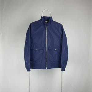May include: A navy blue jacket with a stand-up collar and a silver zipper. The jacket has two front pockets with button closures and ribbed cuffs and hem. The jacket is hanging on a white hanger.