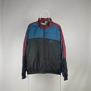 Puede incluir: Chaqueta deportiva Nike vintage en negro, turquesa y burdeos. La chaqueta tiene cremallera completa, cuello alto y el logo de Nike en el pecho. Las mangas son burdeos y el cuerpo está dividido en secciones negras y turquesas.