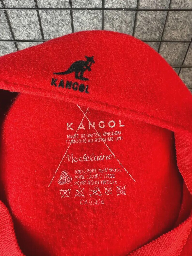 Puede incluir: Boina Kangol roja con el logotipo de la marca, un canguro negro. El interior de la boina muestra el nombre de la marca Kangol e informaci&oacute;n del producto. Fabricado en el Reino Unido.