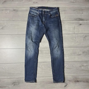 Könnte beinhalten: Blaue Jeans aus Denim mit klassischem Fünf-Taschen-Design. Die Jeans haben eine verwaschene Optik und eine gerade Beinpassform. Die Jeans liegen flach auf einer hellgrauen Holzoberfläche.