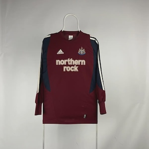 May include: A maroon long-sleeved soccer jersey with navy blue and white accents. The jersey features the Adidas logo, the Newcastle United crest, and the text "northern rock" in gold lettering.