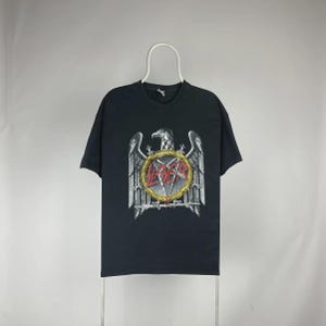 May include: Black t-shirt featuring a large graphic of an eagle with outstretched wings, a pentagram, and the word "SLAYER" in red letters. The design is centered on the front of the shirt. The shirt is hanging on a white hanger.
