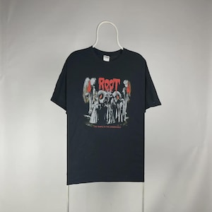 May include: Black t-shirt with a graphic design featuring the word "Root" in red, above a group of figures in white robes. The text "THE TEMPLE IN THE UNDERWORLD" is below the figures. The shirt is hanging on a white hanger.