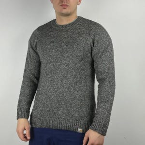 May include: A gray crew neck sweater with long sleeves. The sweater has a textured knit pattern and a small logo patch near the bottom hem. The sweater is made of a thick, warm material, perfect for cooler weather.