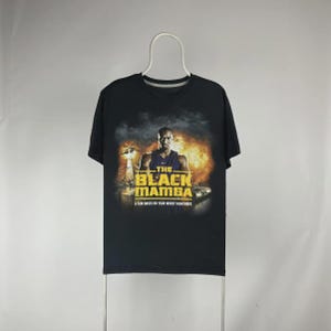 May include: Black t-shirt featuring a graphic of a man with the text "THE BLACK MAMBA" in gold letters. Below the text is the phrase "A FILM BASED ON YOUR WORST NIGHTMARE". The graphic has a fiery background.
