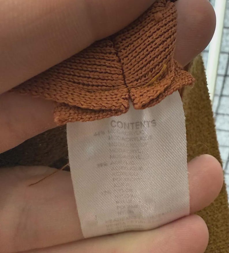 Puede incluir: Primer plano de una tela de punto marr&oacute;n con una etiqueta blanca. La etiqueta dice "CONTENTS" y detalla la composici&oacute;n de la tela, incluyendo acr&iacute;lico. La tela tiene un aspecto texturizado.