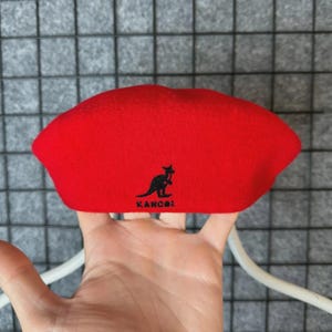 Puede incluir: Un boina roja brillante con el logotipo de Kangol, que presenta un canguro negro. La boina est&aacute; hecha de un material suave y es de estilo cl&aacute;sico. El sombrero es de color liso y es un accesorio de moda popular.