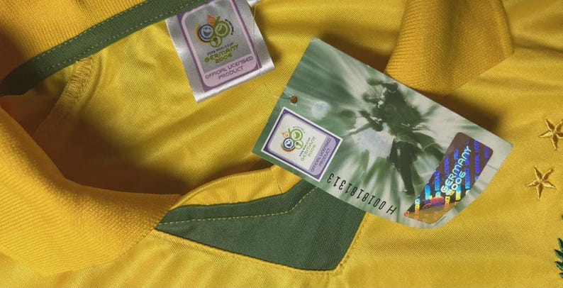 May include: Close-up of a yellow jersey with green accents and tags. The tags feature the 2006 Germany World Cup logo and the text "OFFICIAL LICENSED PRODUCT". A holographic sticker with "GERMANY 2006" is visible.
