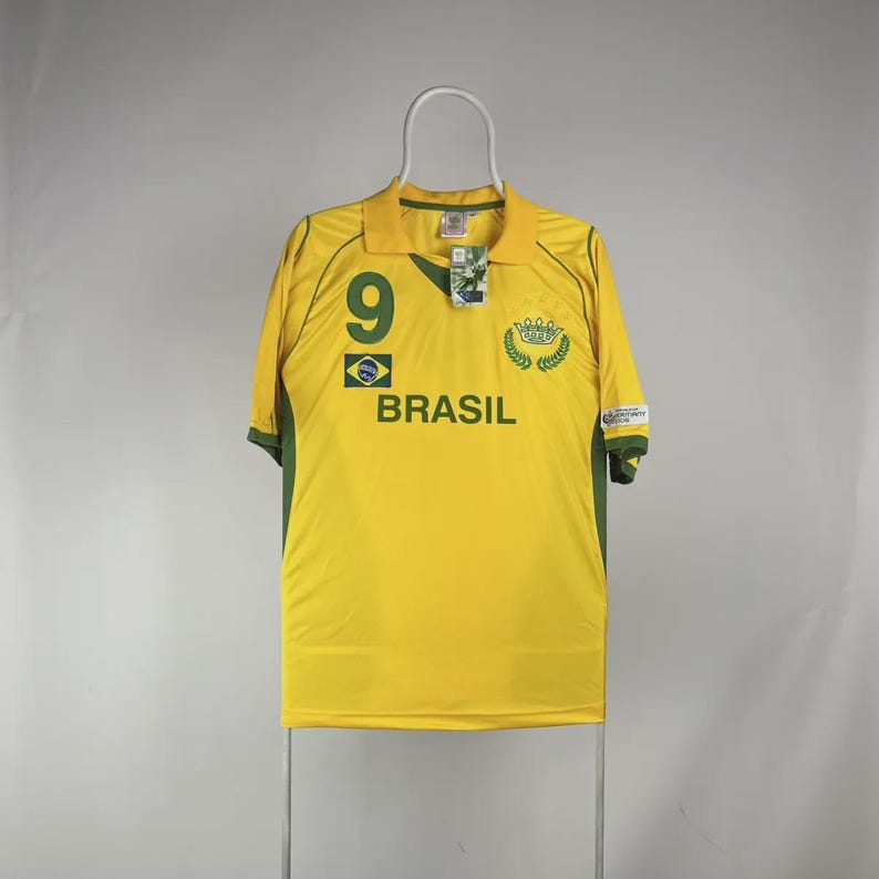 May include: A yellow Brazil soccer jersey with green accents. The jersey features the number 9, the word "BRASIL", and a green and yellow emblem. The shirt is hanging on a white hanger.