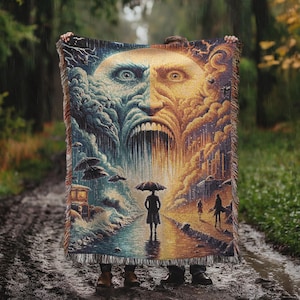 May include: A woven tapestry blanket featuring a surreal, split-face design with a stormy blue side and a sunny yellow side. The artwork depicts a person with an umbrella in the rain, with a city and clouds. The blanket has a fringed edge.