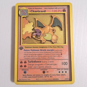 Può includere: Carta collezionabile Pokémon Charizard con bordo giallo. La carta presenta un'illustrazione dettagliata di Charizard, un Pokémon di tipo fuoco. Il testo include "Charizard", "120 PV" e dettagli dell'attacco. Un oggetto da collezione.