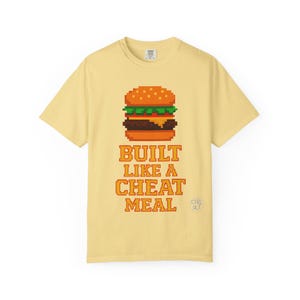May include: Yellow t-shirt with a pixelated image of a hamburger and the text "BUILT LIKE A CHEAT MEAL".