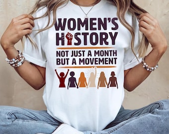 Może przedstawiać: Biała koszulka z napisem "WOMEN'S HISTORY" w ciemnofioletowej czcionce, z grafiką zaciśniętej pięści. Poniżej napis "NOT JUST A MONTH BUT A MOVEMENT". Zawiera rząd stylizowanych postaci kobiecych w różnych kolorach.