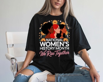 Może przedstawiać: Czarny t-shirt z grafiką na Narodowy Miesiąc Historii Kobiet. Projekt przedstawia trzy profile kobiet otoczone słonecznikami, z napisem "NATIONAL WOMEN'S HISTORY MONTH We Rise Together."