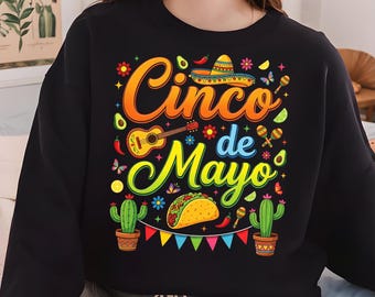 May include: Black sweatshirt with a colorful Cinco de Mayo design. The graphic includes the text "Cinco de Mayo", a sombrero, guitar, maracas, cactus, and a taco. The design is in bright orange, yellow, green, and red.