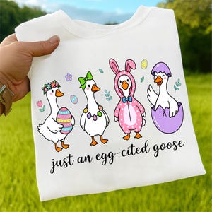 May include: White t-shirt featuring four cartoon geese dressed for Easter. One goose wears a flower crown and holds an Easter egg. Another wears a green bow, and the third is in a pink bunny suit. The text "just an egg-cited goose" is below the geese.