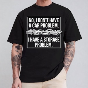 May include: Black t-shirt with the text "NO, I DON'T HAVE A CAR PROBLEM. I HAVE A STORAGE PROBLEM." The shirt features a graphic of four classic cars. The text is in a white, bold font.