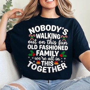 May include: Black t-shirt featuring the text "NOBODY'S WALKING out on this fun OLD FASHIONED FAMILY we're all in THIS TOGETHER" in white, red, and green. The design incorporates candy canes, holly, and bells, indicating a festive theme.