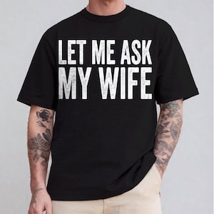 May include: Black t-shirt with the white text "LET ME ASK MY WIFE". The shirt has short sleeves and a crew neck. The text is centered on the front of the shirt.