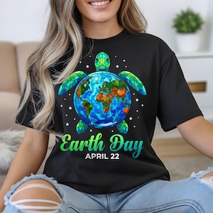 May include: Black t-shirt featuring a colorful graphic of a turtle with the Earth as its shell. The design includes the text "Earth Day APRIL 22" in green and blue. White stars are scattered around the turtle.
