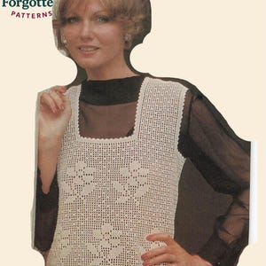 May include: Cream-colored crochet vest with a square neckline and floral design. The vest is part of a vintage pattern from Knot Forgotten Patterns. The vest is worn over a black top.
