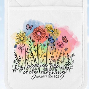 May include: White quilted pot holder with a colorful floral design. The design features yellow, pink, and orange flowers, butterflies, and the text "His mercies are new every morning" from Lamentations 3:23.