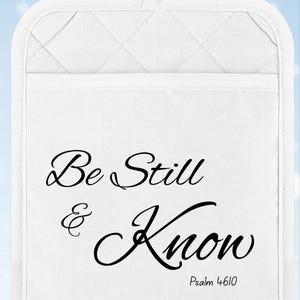 May include: White quilted pot holder with a pocket and a hanging loop. The text "Be Still & Know" is printed in black script, with "Psalm 46:10" below. The background is a light blue with white snowflake accents.
