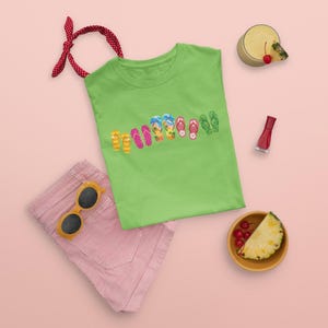 May include: A lime green t-shirt featuring a row of colorful flip-flop illustrations, paired with red and white striped shorts, yellow sunglasses, a red hair ribbon, a glass of pineapple juice with a cherry, and a slice of pineapple.