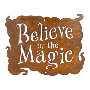 Puede incluir: Un letrero de metal rústico con un acabado marrón oxidado. El letrero presenta letras blancas que dicen "Believe in the Magic".