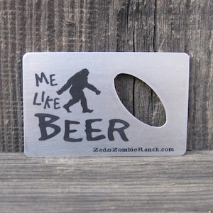 Peut inclure: Un ouvre-bouteille en métal argenté avec une silhouette de Bigfoot et le texte "Me Like Beer". Le bas de l'ouvre-bouteille porte le site Web "ZedsZombieRanch.com" imprimé dessus.
