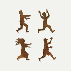 Puede incluir: Cuatro siluetas de zombies de metal oxidado en varias poses. Las siluetas están recortadas y tienen un aspecto desgastado y envejecido.