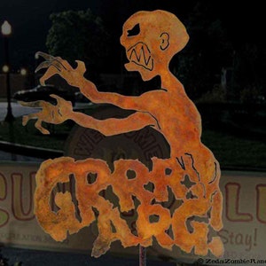 May include: A rusty metal sculpture of a monster with the words "Graveyard" written on its body. The sculpture is in front of a sign that says "Suga-r-Ville" and "Stay!"