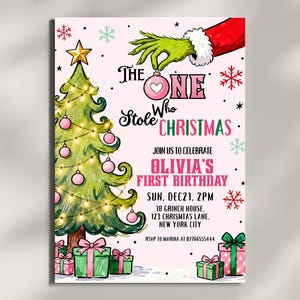 May include: A birthday invitation card featuring a green hand holding a pink ornament above a decorated Christmas tree. Text reads: THE ONE WHO STOLE CHRISTMAS, JOIN US TO CELEBRATE OLIVIA'S FIRST BIRTHDAY, SUN, DEC 21, 2PM, 18 GRINCH HOUSE, NEW YORK CITY.