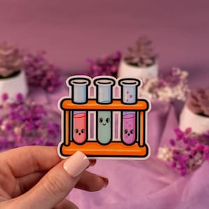 May include: A sticker featuring three cartoon test tubes in an orange rack. The test tubes contain pink, green, and purple liquids, each with a smiling face. The background is a soft purple with small plants.