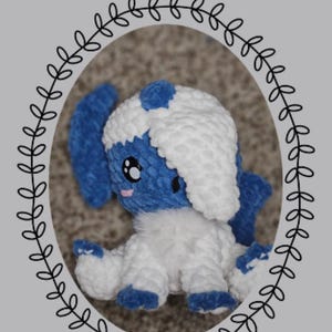 Op de afbeelding: Een handgemaakte gehaakte Absol-knuffel uit de "Chibi Series". De knuffel heeft blauw en wit garen, met grote zwarte ogen en een roze mond. De afbeelding bevat de tekst "Eevelutionary Crochet" en "Absol".