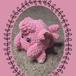 Könnte beinhalten: Handgefertigtes, rosa gehäkeltes Clefairy-Plüschtier aus der "Chibi-Serie" mit braunen Akzenten an den Ohren. Das Plüschtier befindet sich in einem schwarzen Ovalrahmen mit Blättermuster. Der Hintergrund ist rosa mit dem Text "Eeveelutionary Crochet" und "Clefairy."