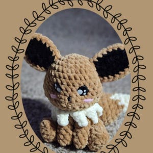 May include: A crocheted Eevee plushie from the "Chibi Series" with brown, black, white, and pink details. The plushie is inside a brown oval with a leafy border. The text "Eevee" is above the plushie.
