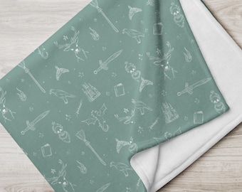 May include: A soft, green fleece throw blanket with a white pattern of various magical symbols, including a dragon, a castle, a sword, a book, a broom, a deer, and a phoenix.