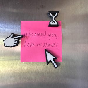 May include: A pink sticky note with the handwritten message "We need you, takes us home!" is affixed to a metallic surface. Pixelated cursor, hand, and hourglass magnets are also attached.