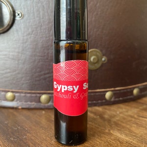 May include: A small brown glass roller bottle with a black cap. The label is red with white text that reads "Gypsy Soul Patchouli & Grapefruit".