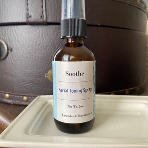 May include: A brown glass bottle with a black spray top and a white label that reads "Soothe Facial Toning Spray Net Wt. 2 oz. Lavender & Frankincense".