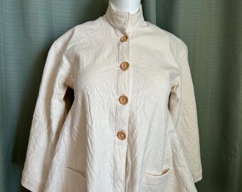 May include: Off-white quilted jacket with a mandarin collar and wooden buttons. The jacket has two front pockets and long sleeves. The fabric has a subtle textured pattern. The jacket is displayed on a mannequin.
