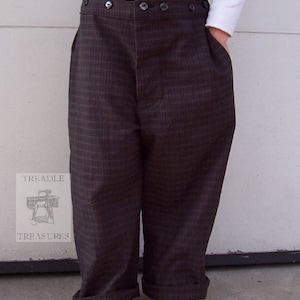 May include: Brown plaid trousers with a high waist and button closure. The trousers have a relaxed fit with cuffed hems and pockets. The fabric has a subtle grid pattern in shades of brown and blue. The trousers are shown on a person.