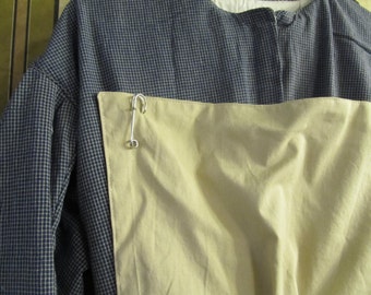 May include: A blue and white checkered shirt with a light tan panel across the chest. A silver metal clasp secures the panel to the shirt. The shirt has a simple, classic design.