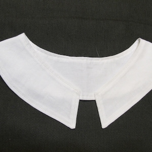 May include: A white, detachable collar with a classic design. The collar is made of a crisp, white fabric and features a pointed front and a curved back. The edges are neatly stitched, and the collar is set against a dark background.