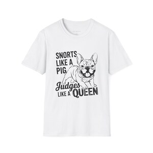 May include: White t-shirt with a black and white illustration of a French bulldog. The text "Snorts like a pig. Judges like a queen" is printed on the shirt.