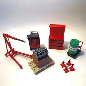 May include: A miniature garage set featuring a red engine hoist, a black and red rolling tool cabinet with a gray toolbox, a red stationary tool chest, a gray engine block on a brown box and pallet, a green Castrol oil drum, and four red jack stands.