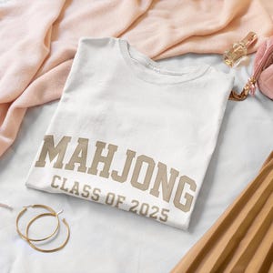 May include: White t-shirt with the text "Mahjong Class of 2025" in brown lettering.
